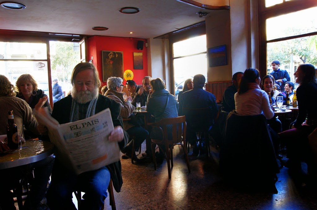 Locals enjoying coffee and newspapers at a cafe in Barcelona during a cold day.
