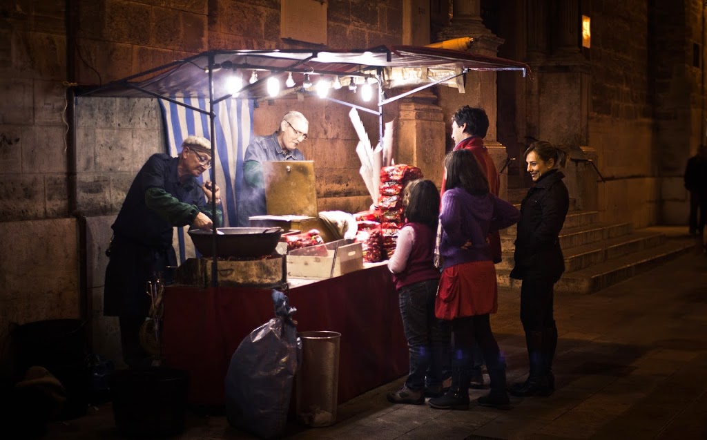 Vendors roasting chestnuts over hot coals during a cold night, a common sight in Barcelona in the winter.